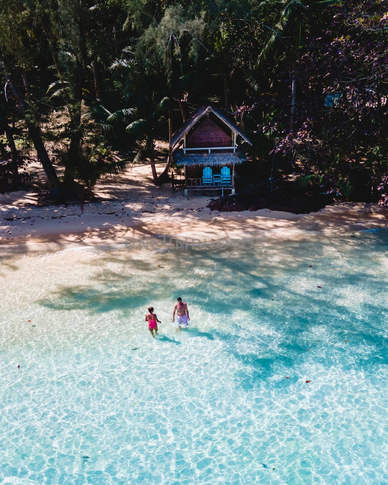 Koh Wai Island Thailand is a tinny tropical Island near Koh Chang. wooden bamboo hut bungalow on the beach. a young couple of men and women swimming in the blue ocean on a tropical Island in Thailand