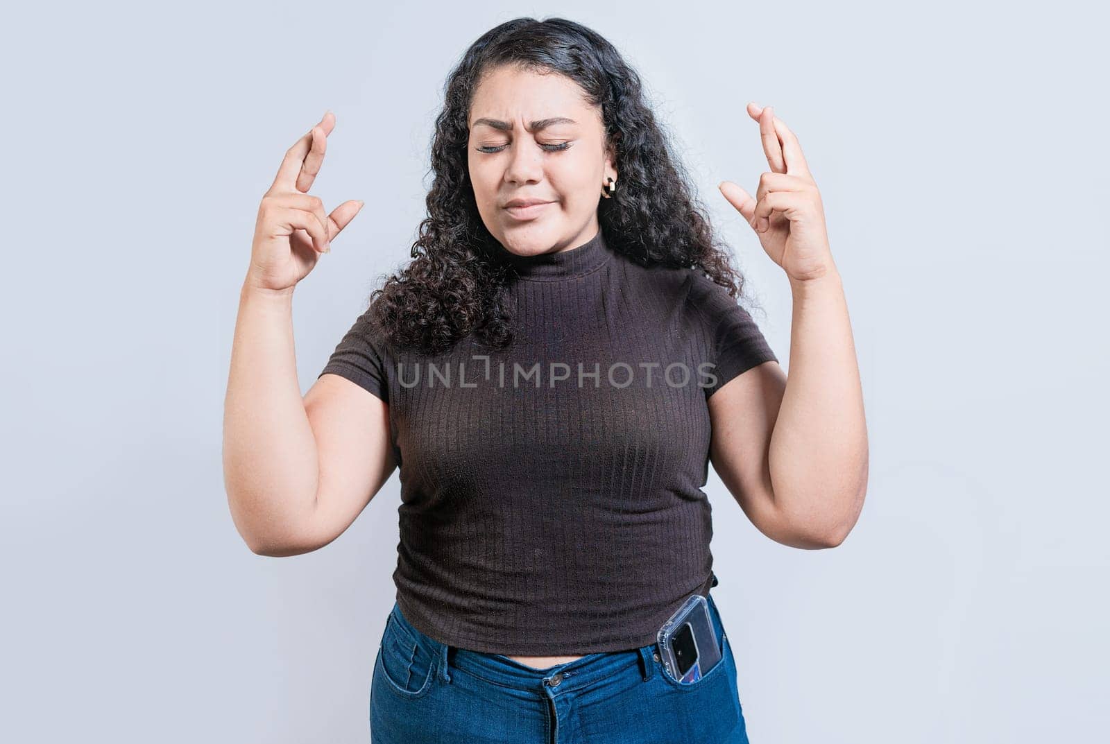 Latin girl crossing fingers making a wish. Smiling young woman making a wish with hopeful gesture by isaiphoto