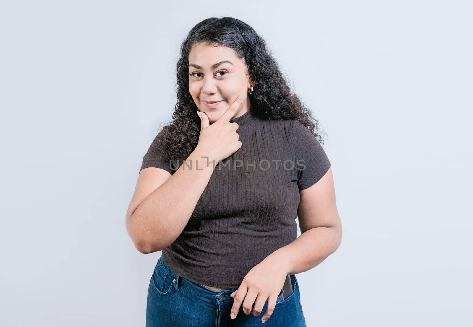 Beautiful latin girl thinking with hand on chin. Young woman rubbing chin with a doubtful expression by isaiphoto