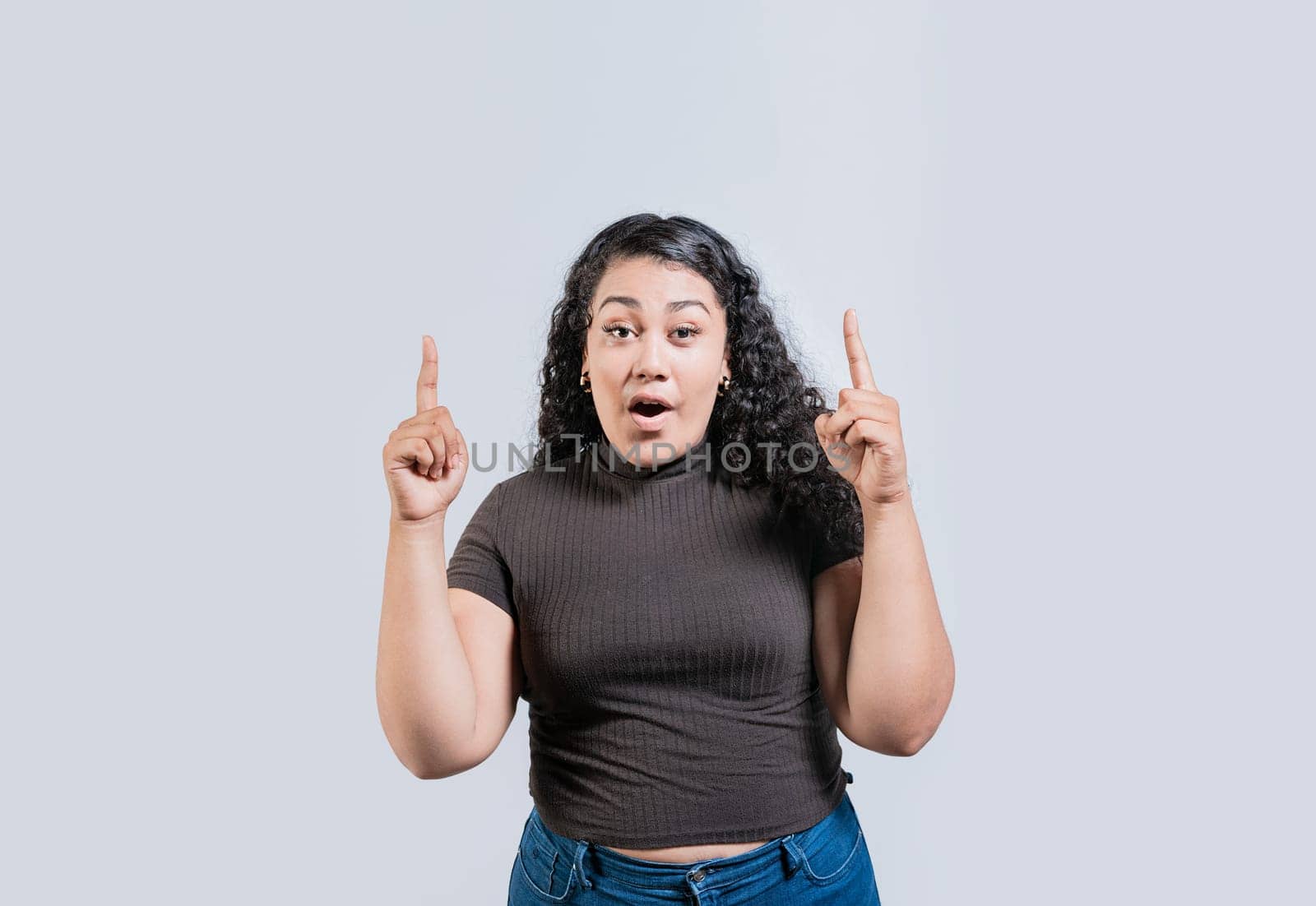 Young latin girl amazed pointing a promotion up isolated. Young curly-haired woman pointing up. Latin people pointing up by isaiphoto