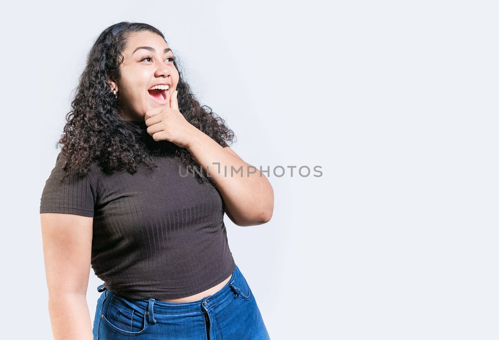 Happy young woman holding chin looking at an advertisement to side. Excited latin woman with hand on chin looking a promo to the side isolated by isaiphoto