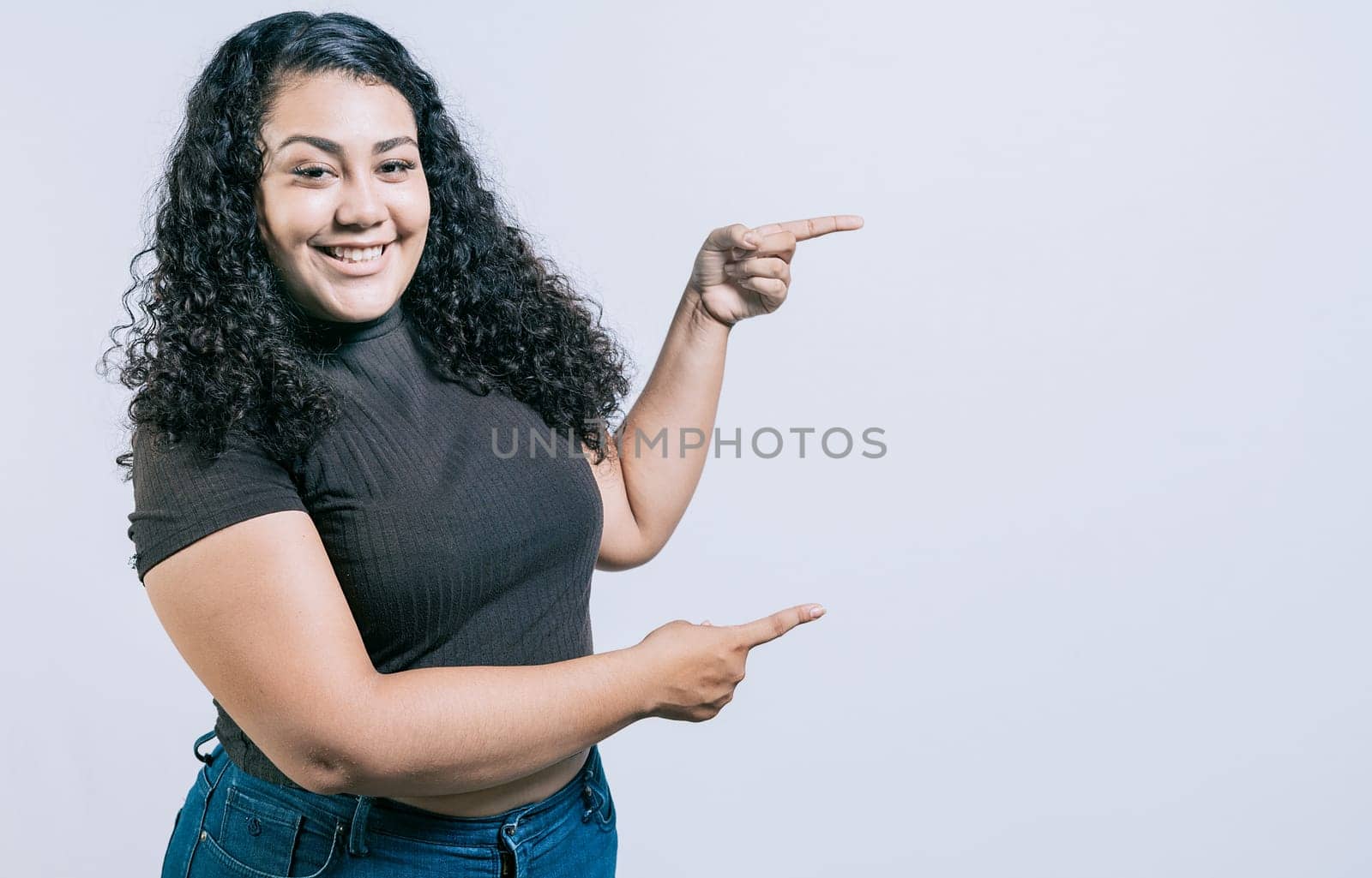 Smiling young caucasian woman pointing a promotion isolated. Cheerful girl pointing an offer isolated. Young girl pointing to a banner to the side