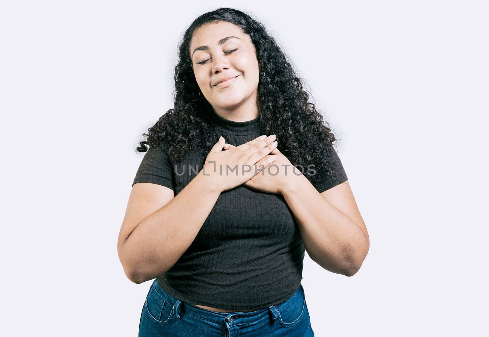 Positive latin girl with hands on chest. Grateful young woman with hands on chest. Grateful teenage girl smiling with hands on chest isolated by isaiphoto