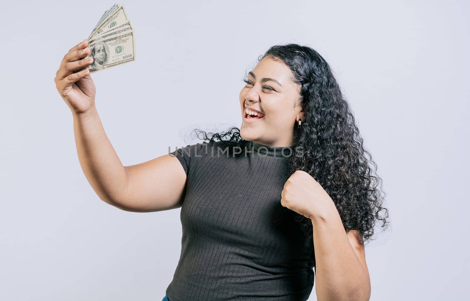 Victorious young woman holding money celebrating isolated. Excited latin girl holding dollar cash isolated
