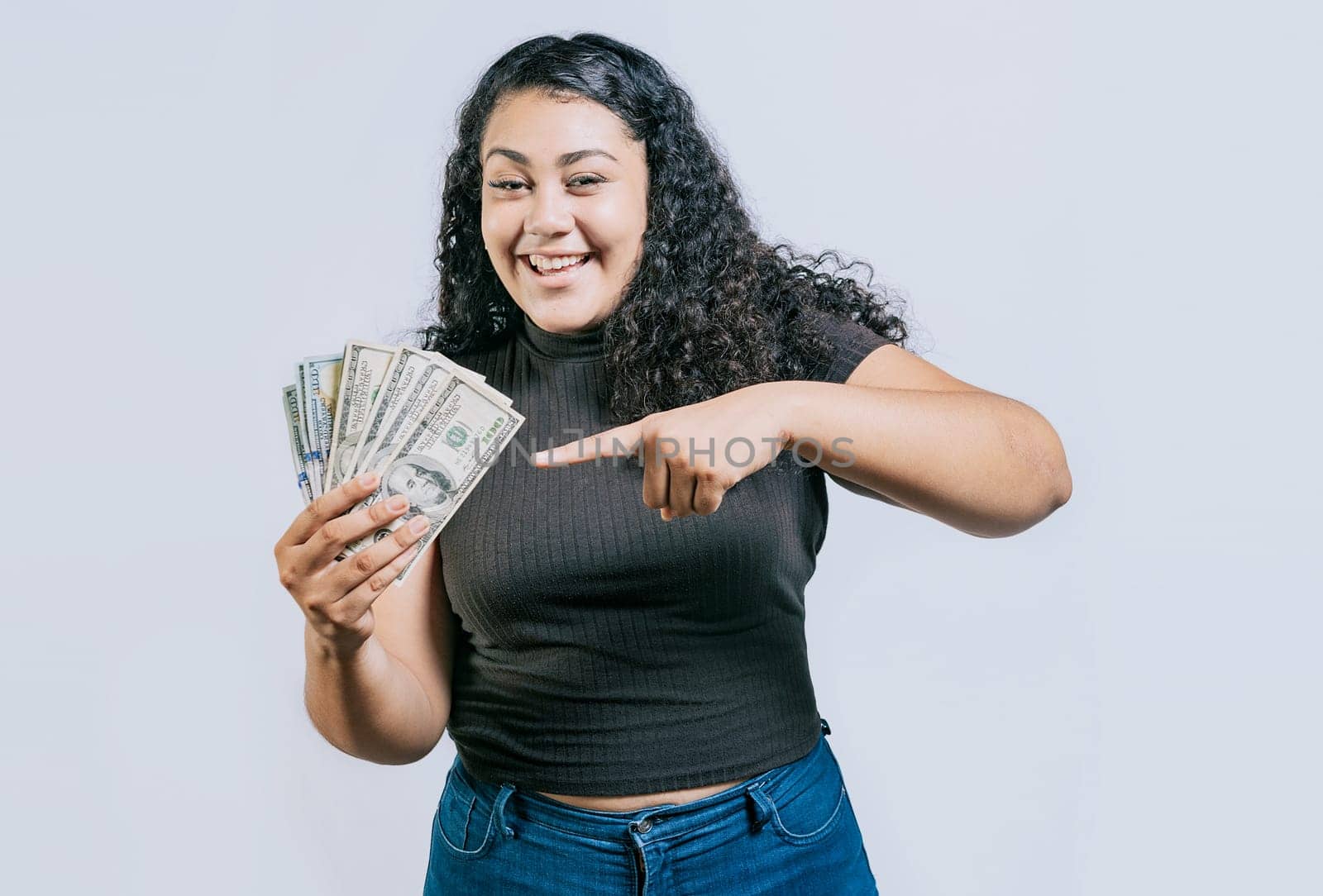 Attractive latin girl holding and pointing money. Smiling young woman holding and pointing money isolated. Latin people holding money