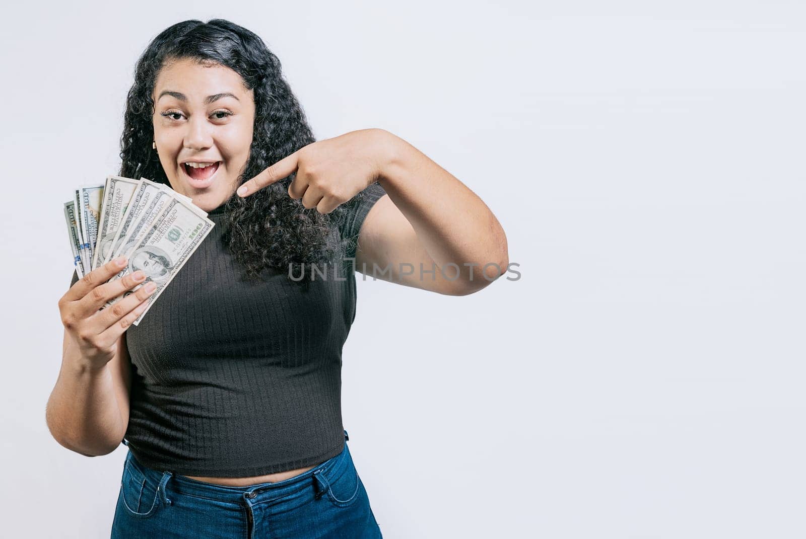 Smiling young woman holding and pointing money isolated. Attractive latin girl holding and pointing money. Latin people holding money by isaiphoto