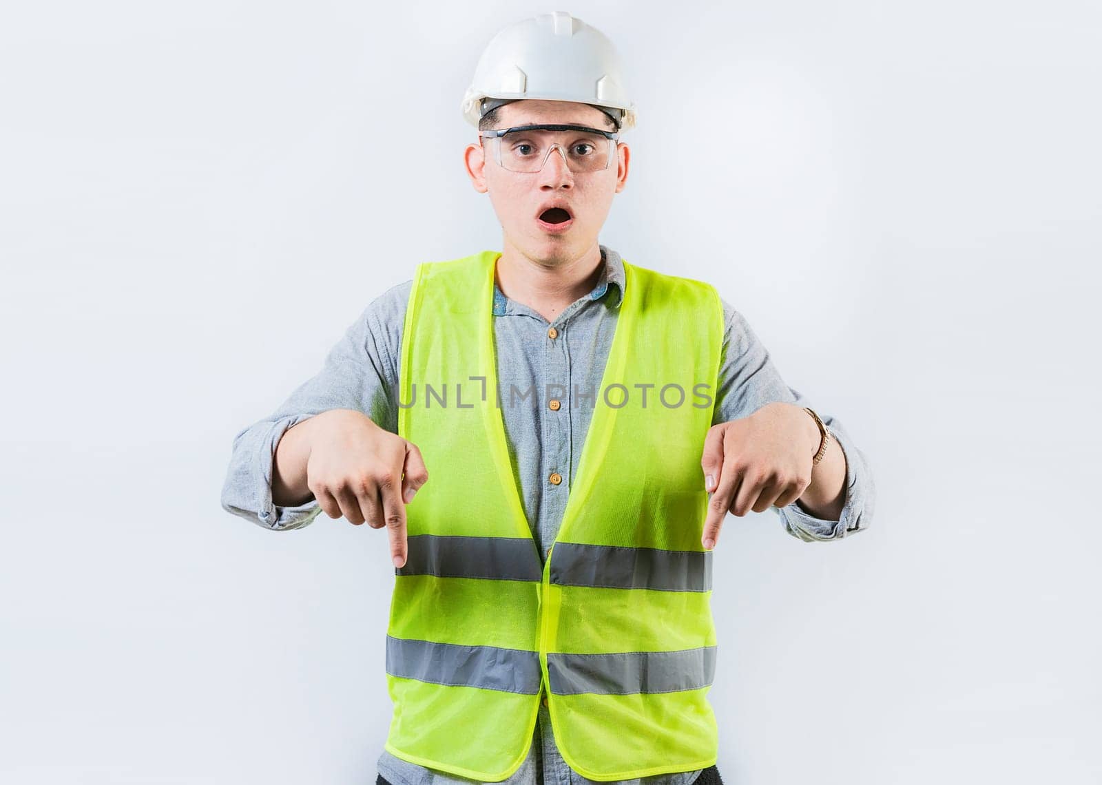 Surprised engineer pointing down advertising space isolated. Astonished male engineer pointing down an advertising space by isaiphoto