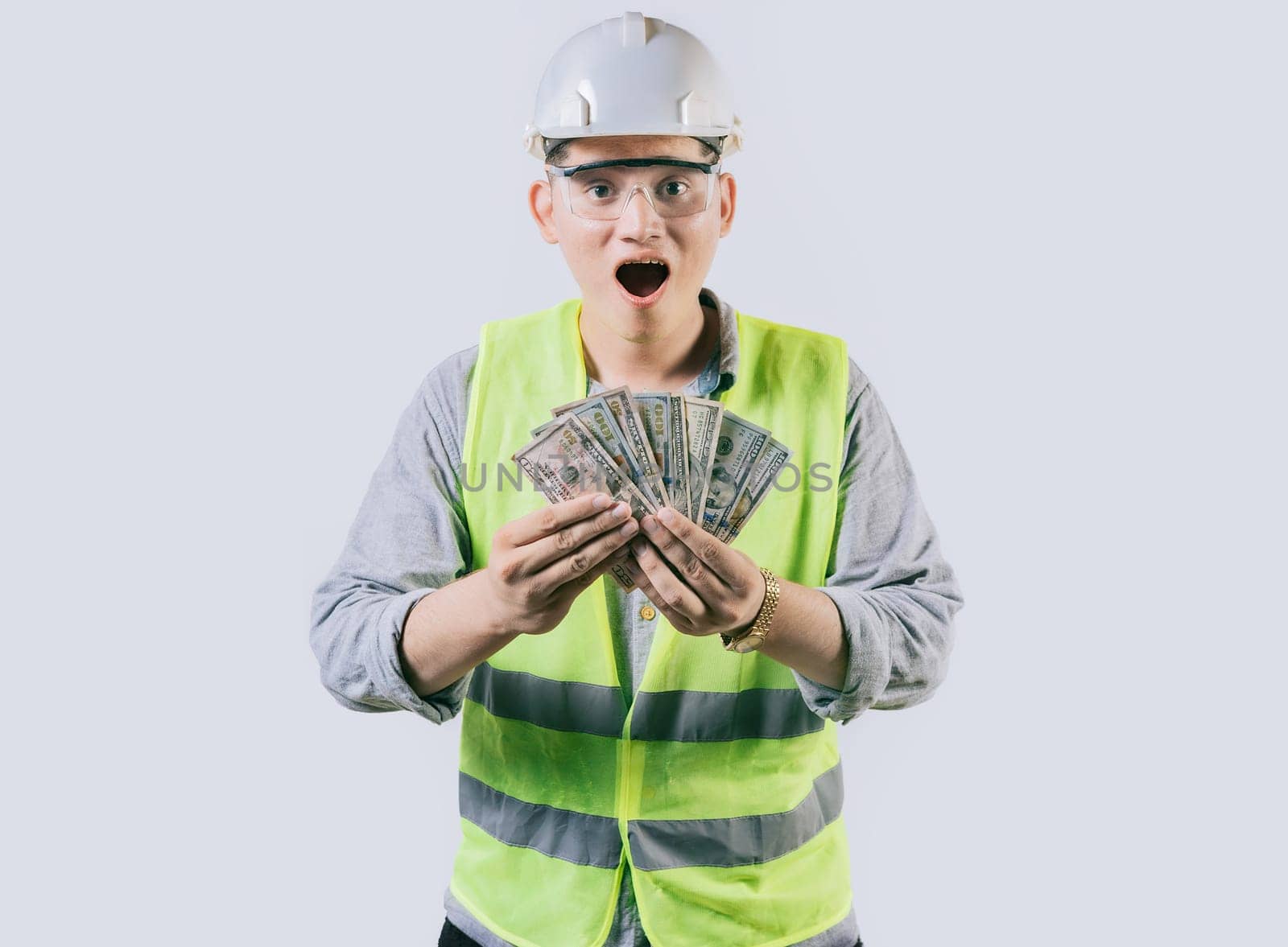 Surprised engineer in helmet holding money isolated. Amazed male engineer holding banknotes on isolated background by isaiphoto