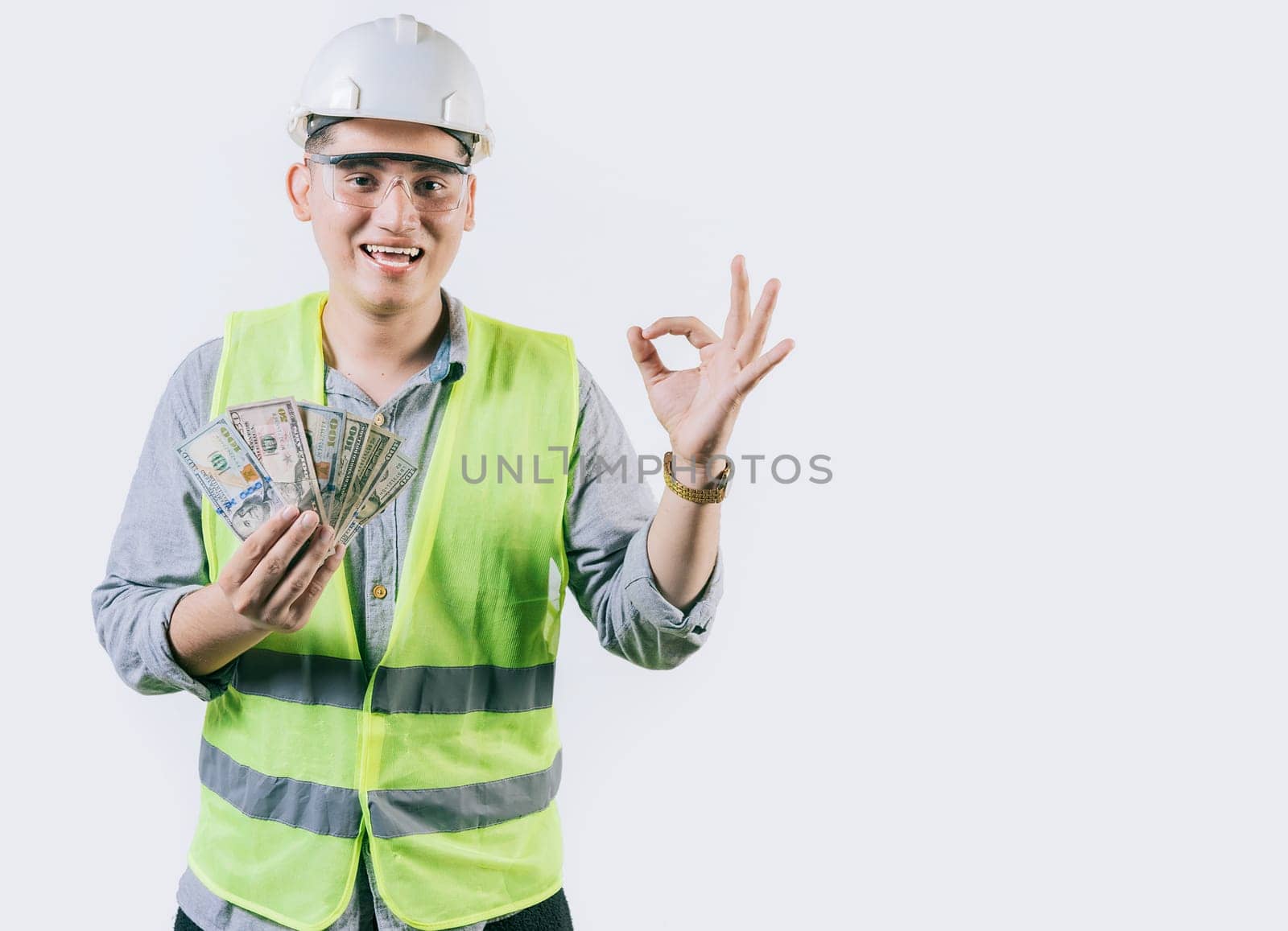 Smiling engineer constructor holding money gesturing ok isolated. Latin engineer showing money making gesture ok isolated by isaiphoto