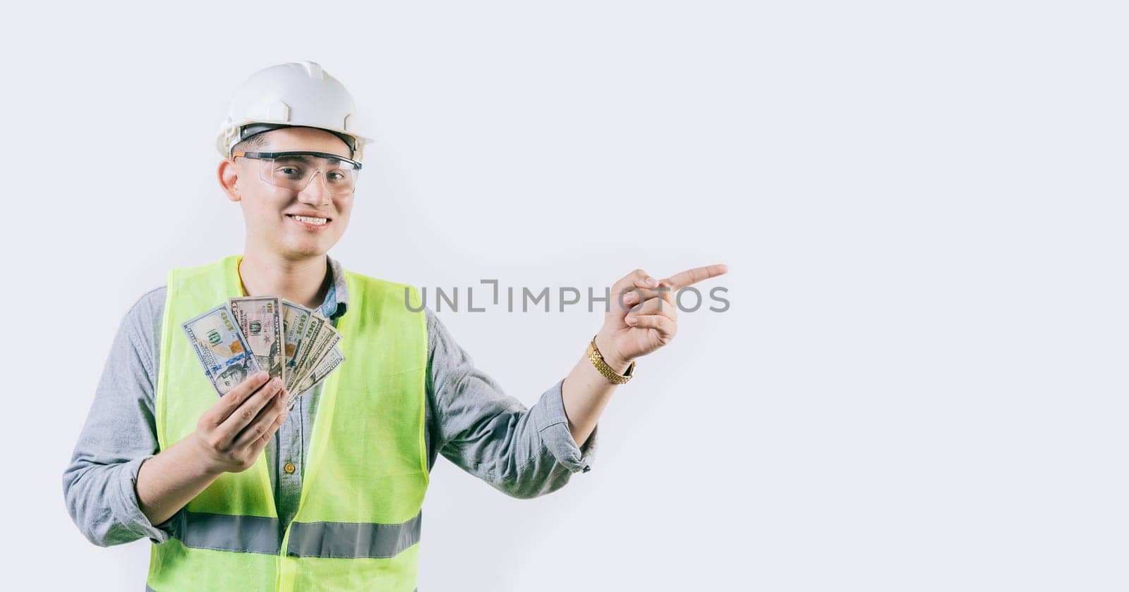 Smiling young engineer holding money pointing aside isolated. Handsome male engineer showing money pointing an advertisement isolated by isaiphoto