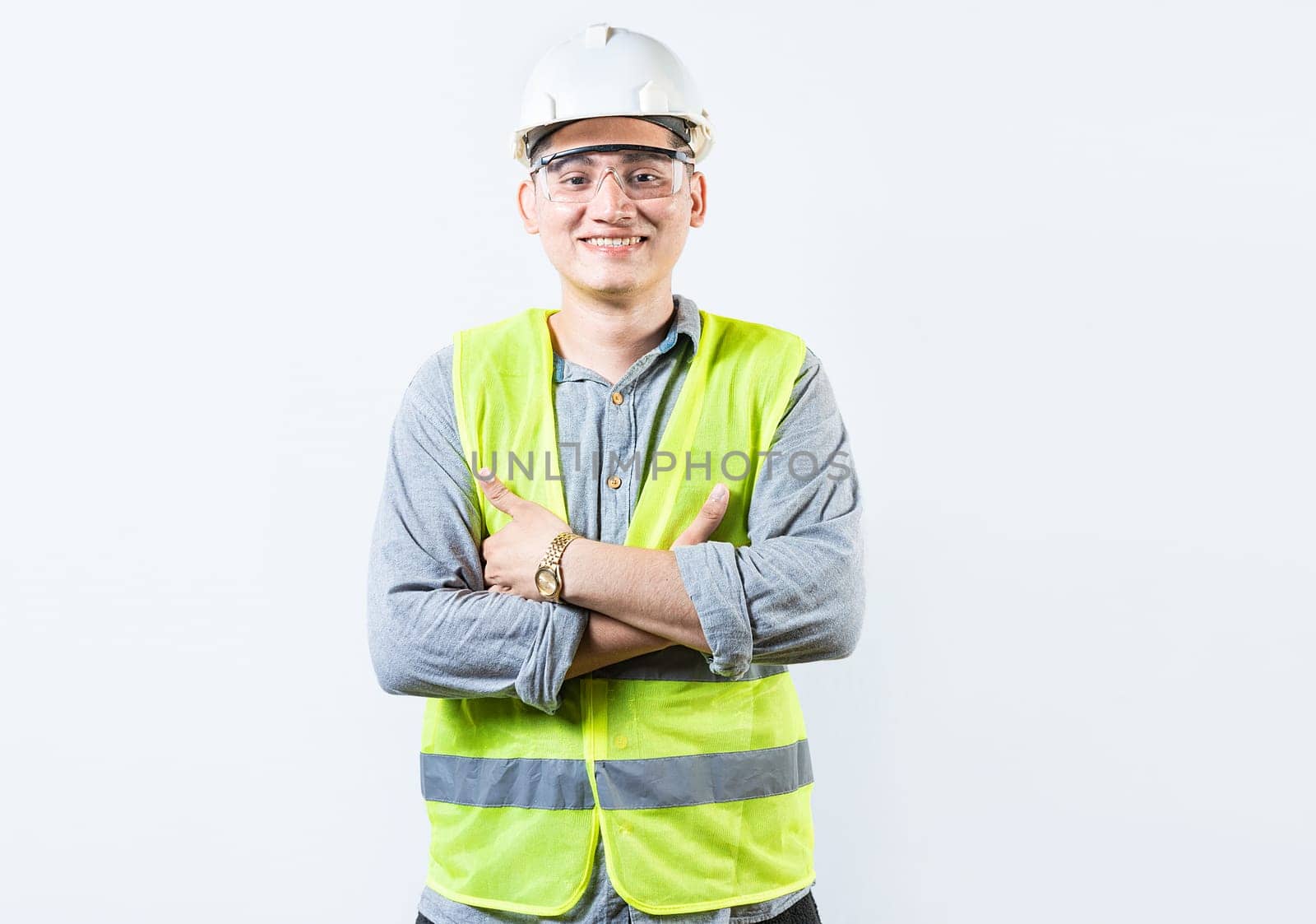 Portrait of handsome and smiling engineer with crossed arms isolated. Portrait of a young cheerful engineer in helmet and vest isolated.