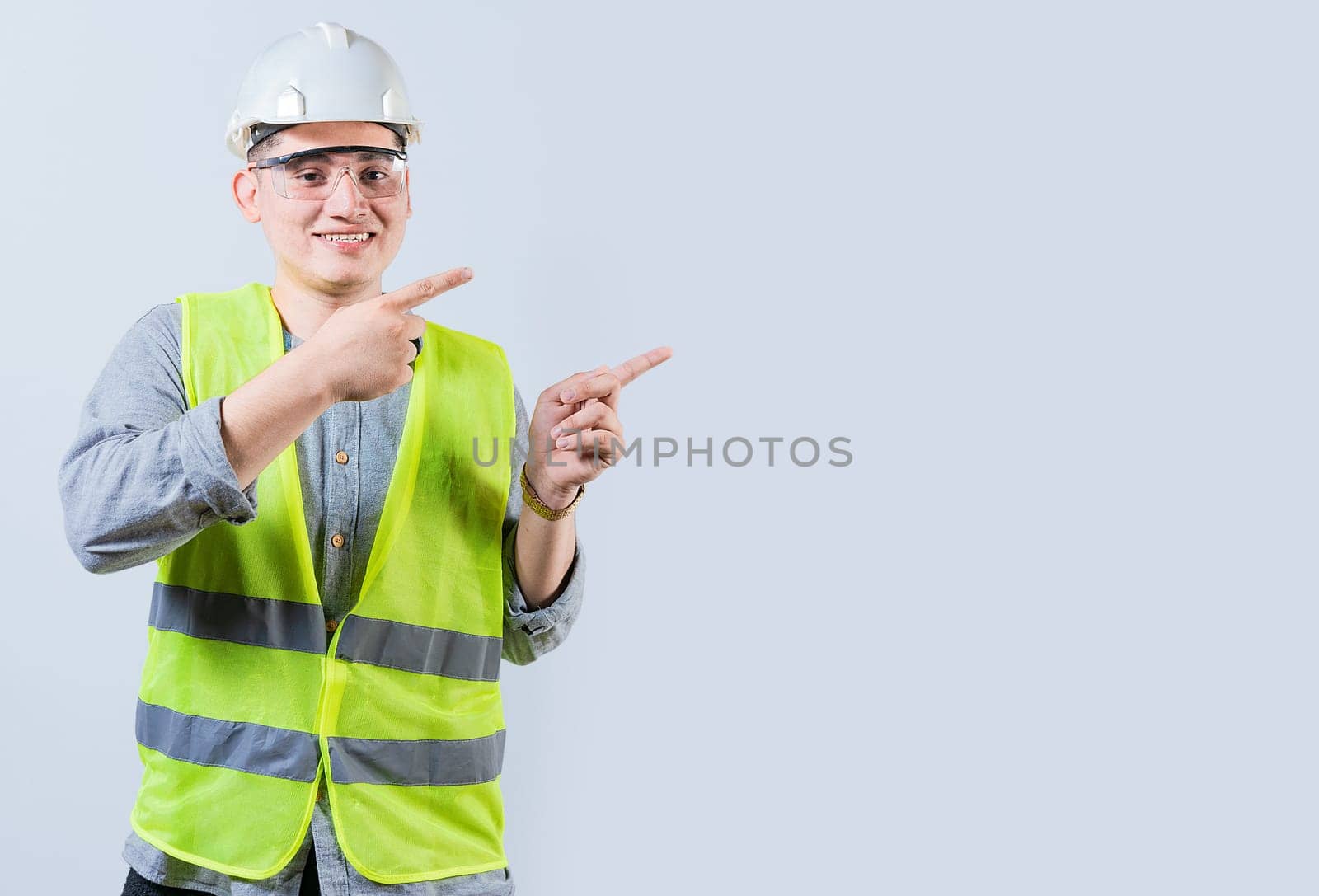 Cheerful engineer with helmet pointing aside isolated. Handsome engineer pointing an advertisement isolated by isaiphoto