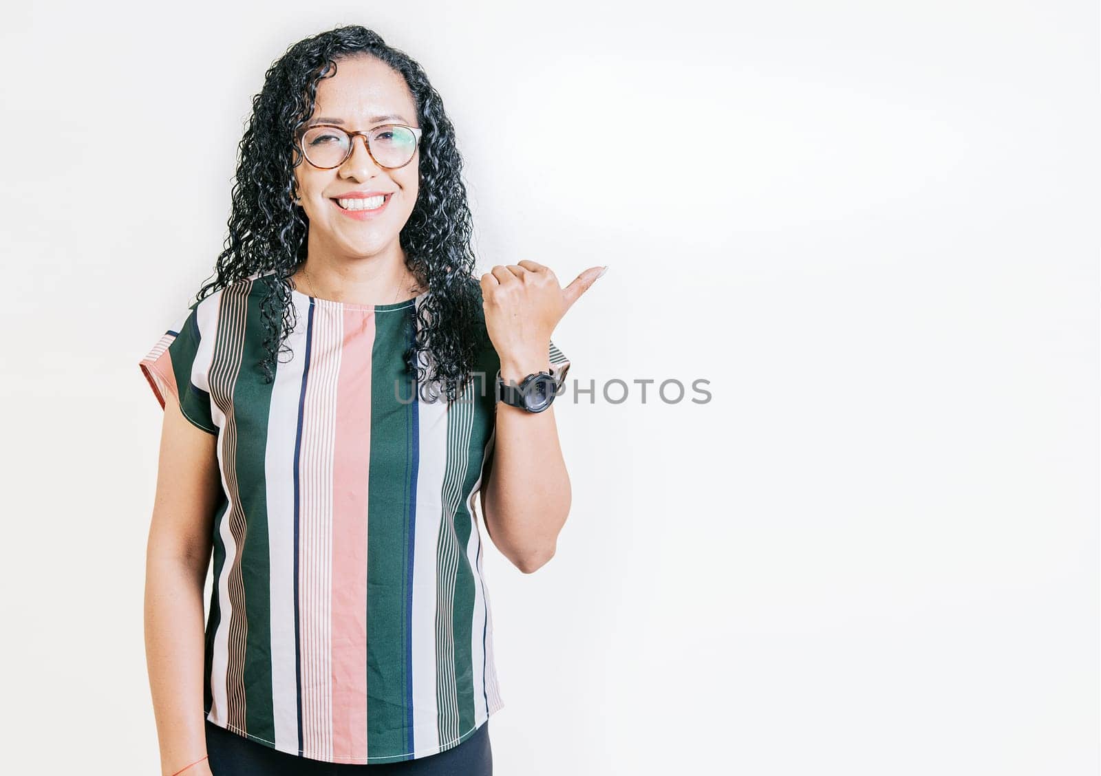 Smiling latin people pointing to a banner to the side. Happy latin woman recommending with fingers isolated. Cheerful curly haired girl pointing an offer by isaiphoto