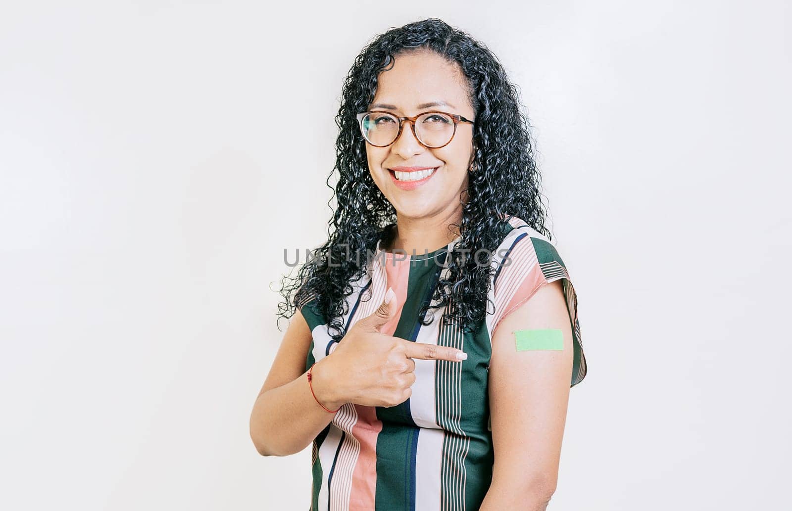 Latin woman pointing at the bandage on her vaccinated arm isolated. Smiling woman pointing at her vaccinated arm by isaiphoto