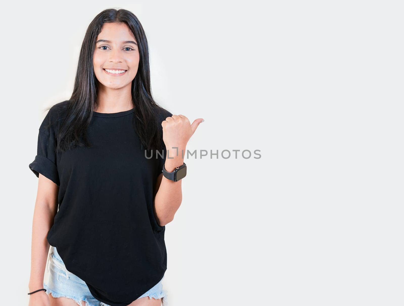 Friendly young girl pointing to a banner to the side. Happy latin woman recommending a promo isolated. Cheerful latin girl pointing an offer isolated by isaiphoto