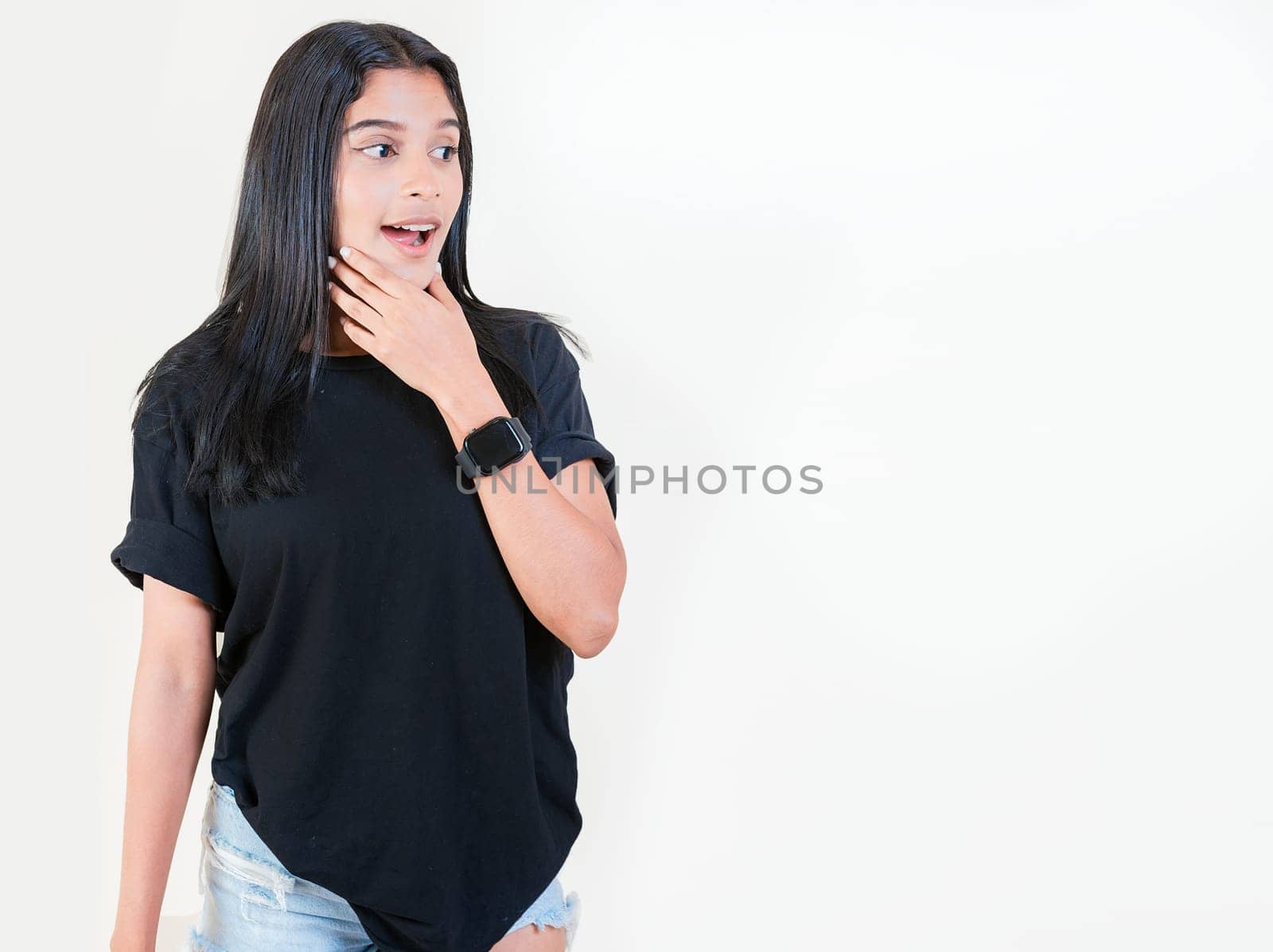 Shocked young girl looking at a promotion to the side. Amazed people with hand on chin looking at blank space. Surprised teen girl looking at an advertisement to side by isaiphoto