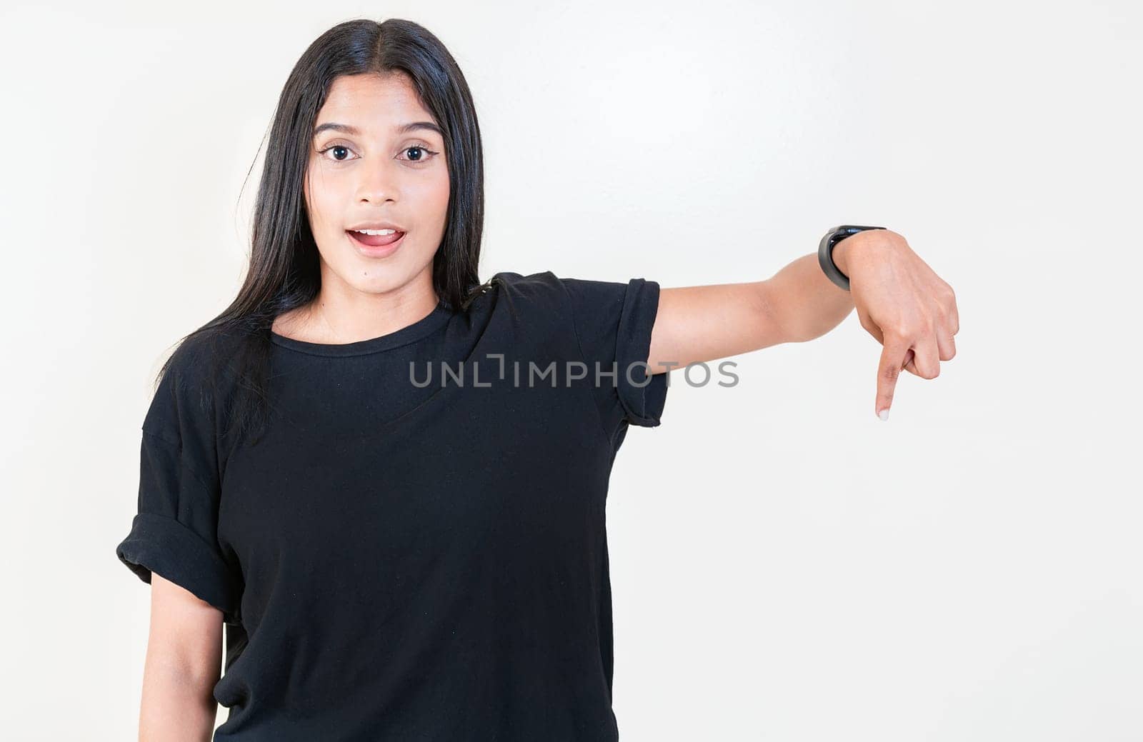 Amazed latin girl pointing down an advertisement. Cheerful girl pointing advertising down. Latin people pointing down at a banner by isaiphoto