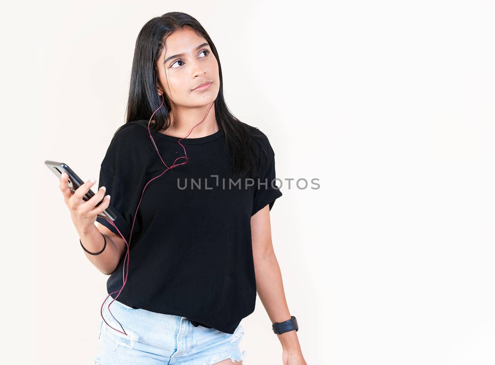 Portrait of beautiful girl listening to music with smartphone isolated. Happy latin gir listening to music with cell phone. Latin girl enjoying music with phone isolated by isaiphoto