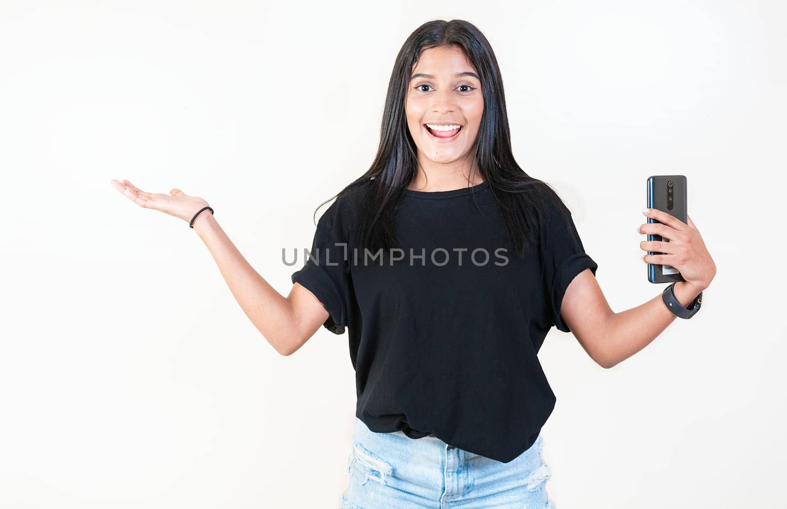 Happy latin girl holding phone and looking at camera. Cheerful young girl holding smartphone and smiling at camera by isaiphoto