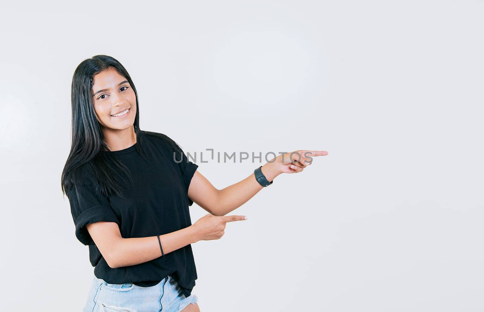 Cheerful teen girl pointing an offer isolated. Beautiful young girl pointing to a banner to the side. Happy latin woman pointing a promo isolated by isaiphoto