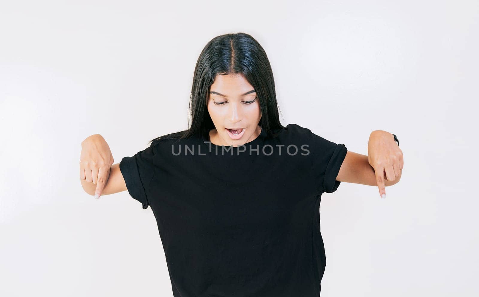 Amazed girl pointing at advertising down isolated. Surprised latin girl pointing blank space down by isaiphoto