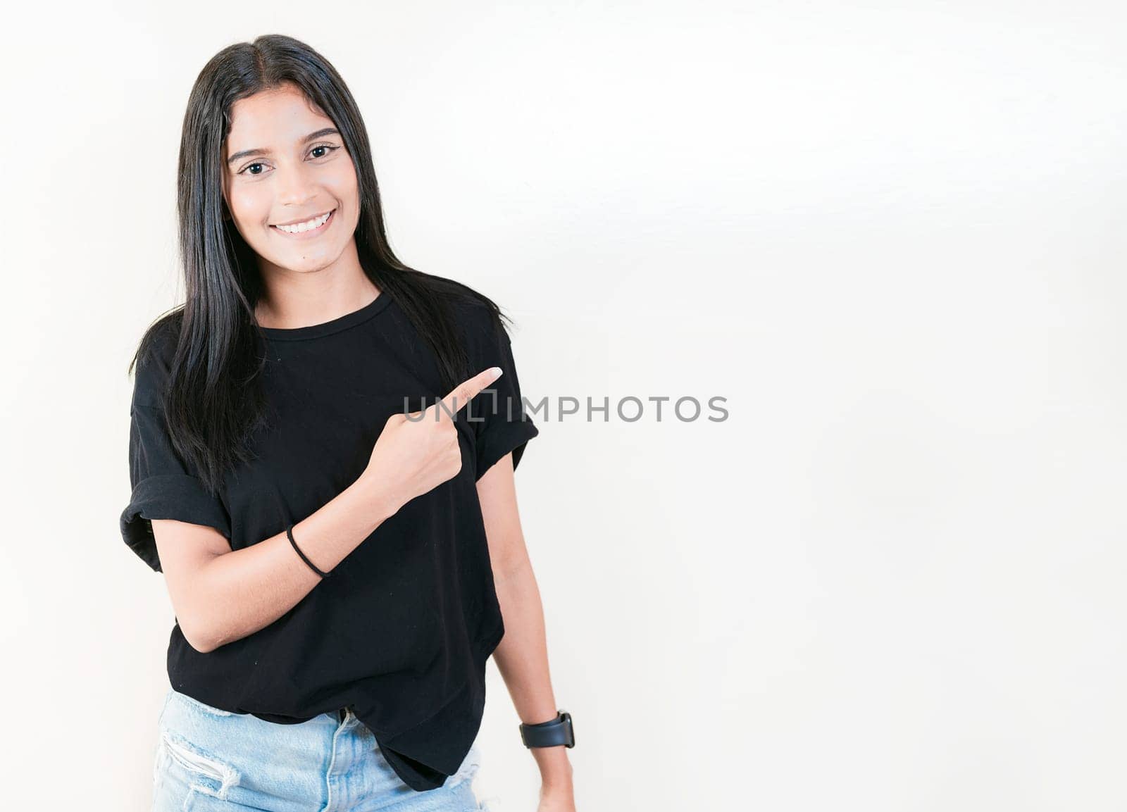 Smiling teenage girl pointing side with hand. Cheerful latin girl pointing an offer isolated. Happy teenager pointing a promo isolated by isaiphoto