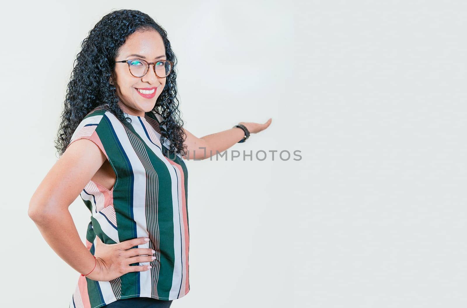 Smiling young afro woman welcoming you isolated. Happy afro girl pointing back presenting a product isolated. Cheerful people pointing a promotion with her palm by isaiphoto