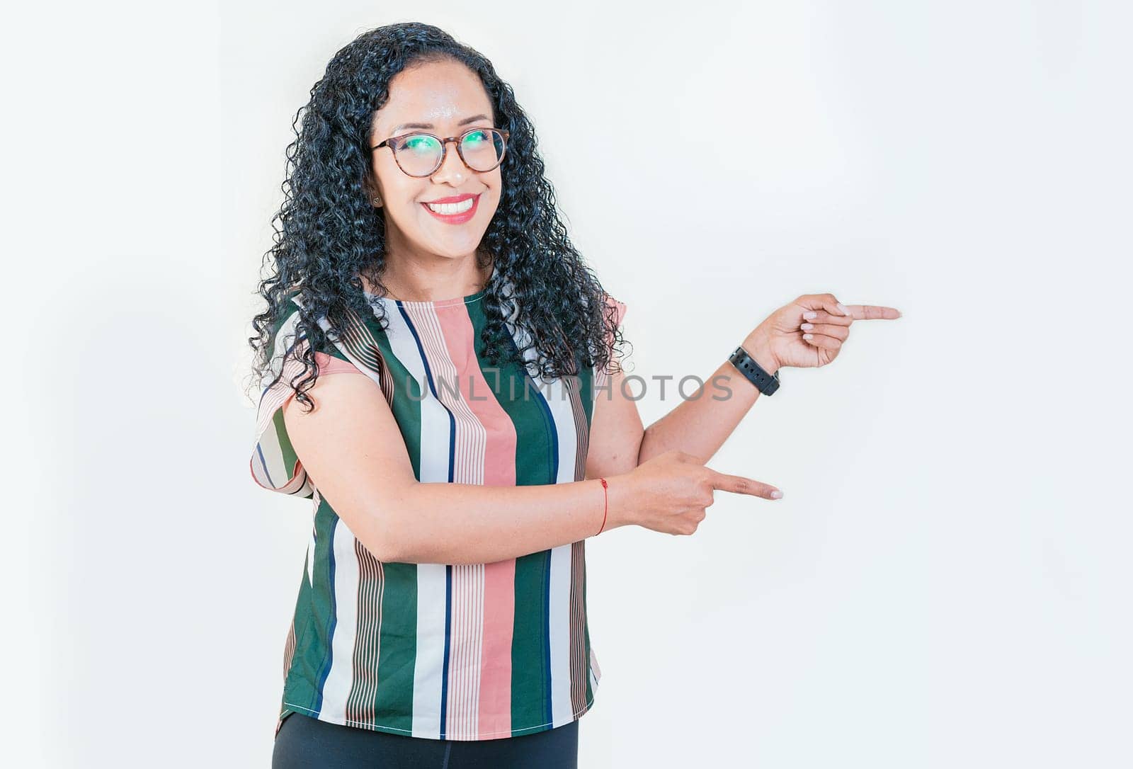 Cheerful afro girl pointing an offer isolated. Beautiful latin girl pointing to a banner to the side. Happy young afro woman pointing a promotion at side by isaiphoto