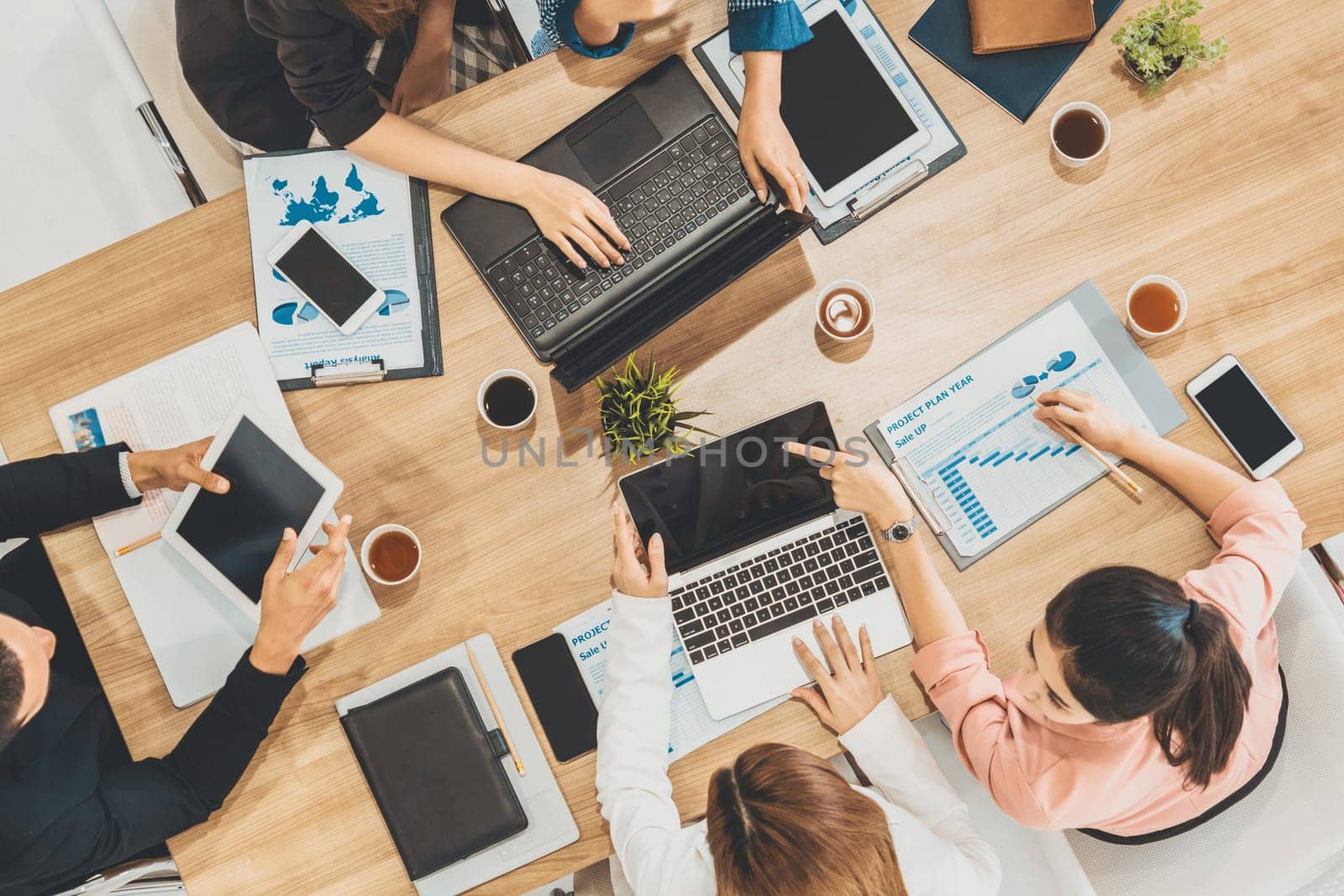 Top view of businessman executive in group meeting with other businessmen and businesswomen in modern office with laptop computer, coffee and document on table. People corporate business team uds