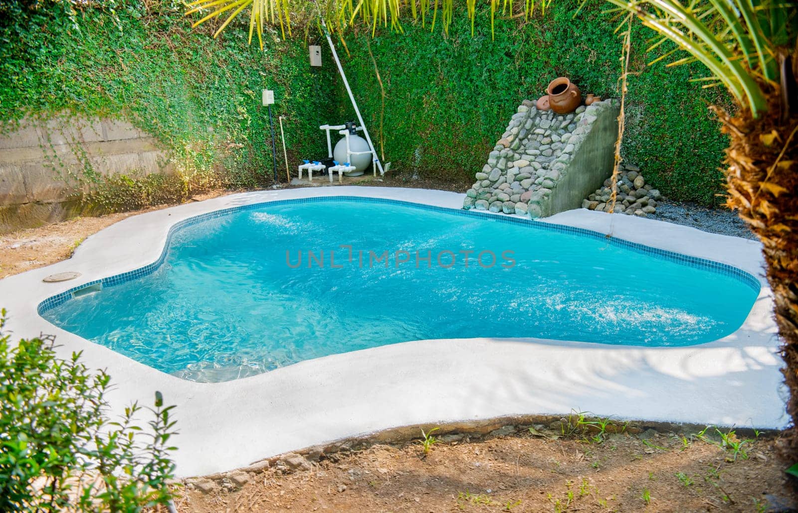 Homemade swimming pool in a garden. Swimming pool designs for the home. Crystal water home pool surrounded by a garden. Home swimming pool maintenance concept by isaiphoto