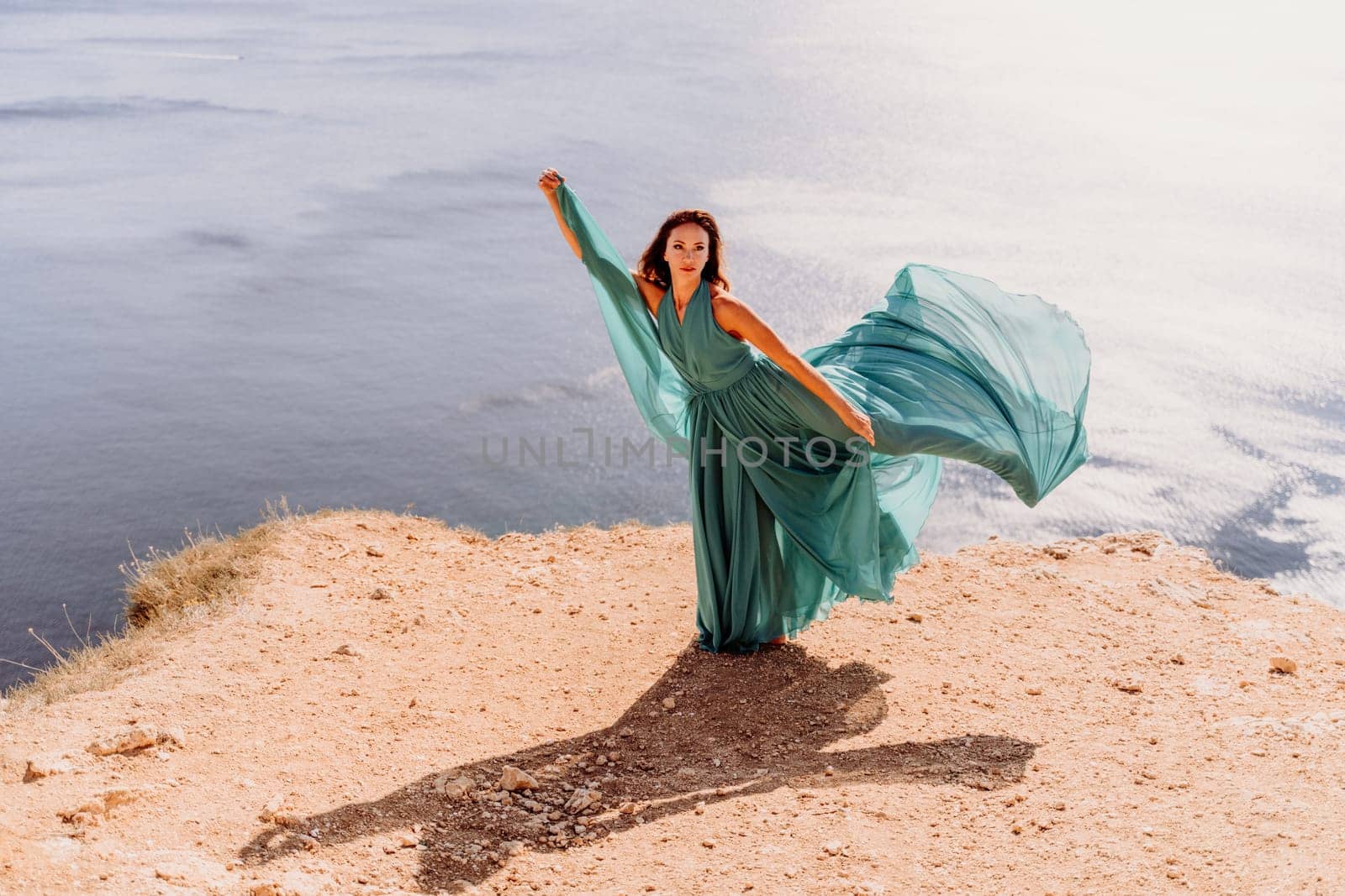 Woman green dress sea. Female dancer posing on a rocky outcrop high above the sea. Girl on the nature on blue sky background. Fashion photo