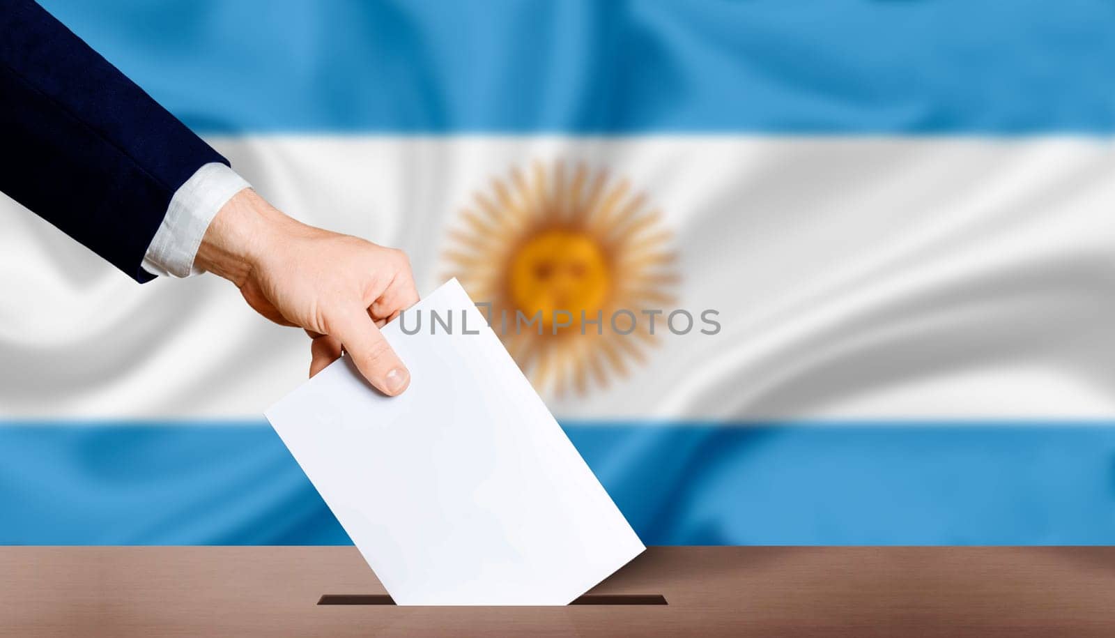 Hand holding ballot in voting ballot box with Argentina flag in background. Hand man puts ballot paper in voting box on Argentina flag background. Argentina electoral elections, concept by isaiphoto