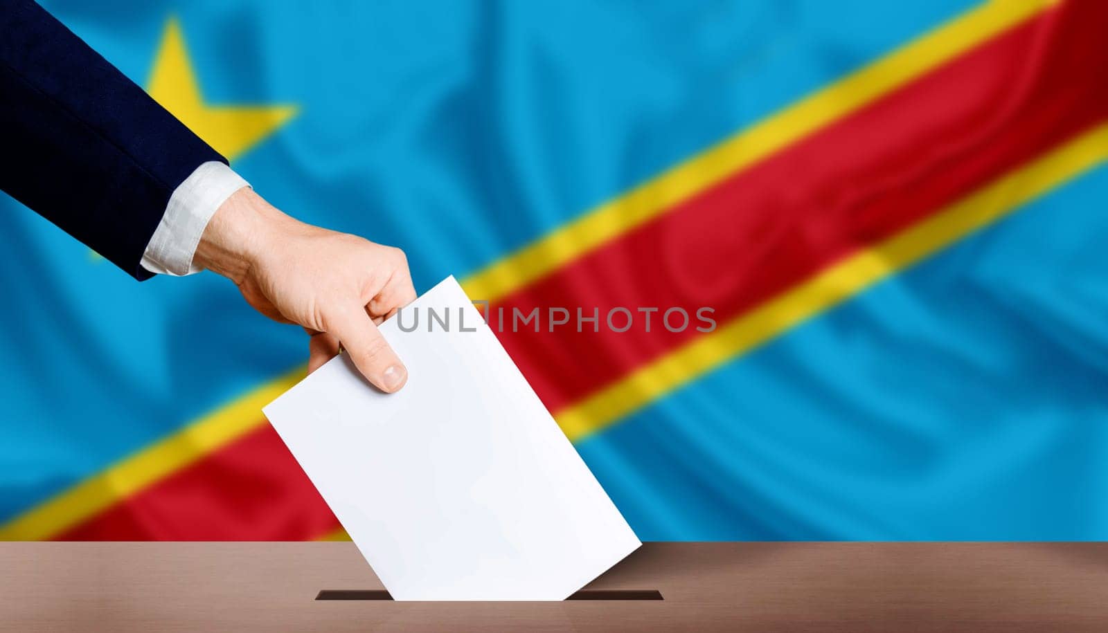 Hand holding ballot in voting ballot box with Democratic Republic of the Congo flag in background. Presidential elections of the democratic republic of the congo by isaiphoto