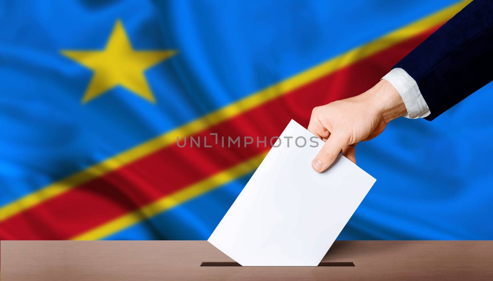 Presidential elections of the Democratic Republic of the Congo. Hand holding ballot in voting ballot box with Democratic Republic of the Congo flag in background by isaiphoto