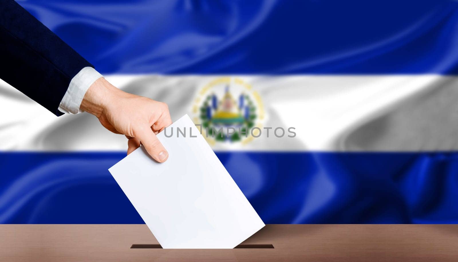 El Salvador presidential elections concept. Hand holding ballot in voting ballot box with El Salvador flag in background by isaiphoto