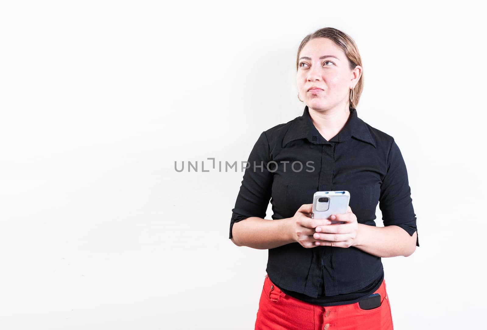 Thoughtful young woman holding phone isolated. Pensive latin girl holding smart phone on white background by isaiphoto