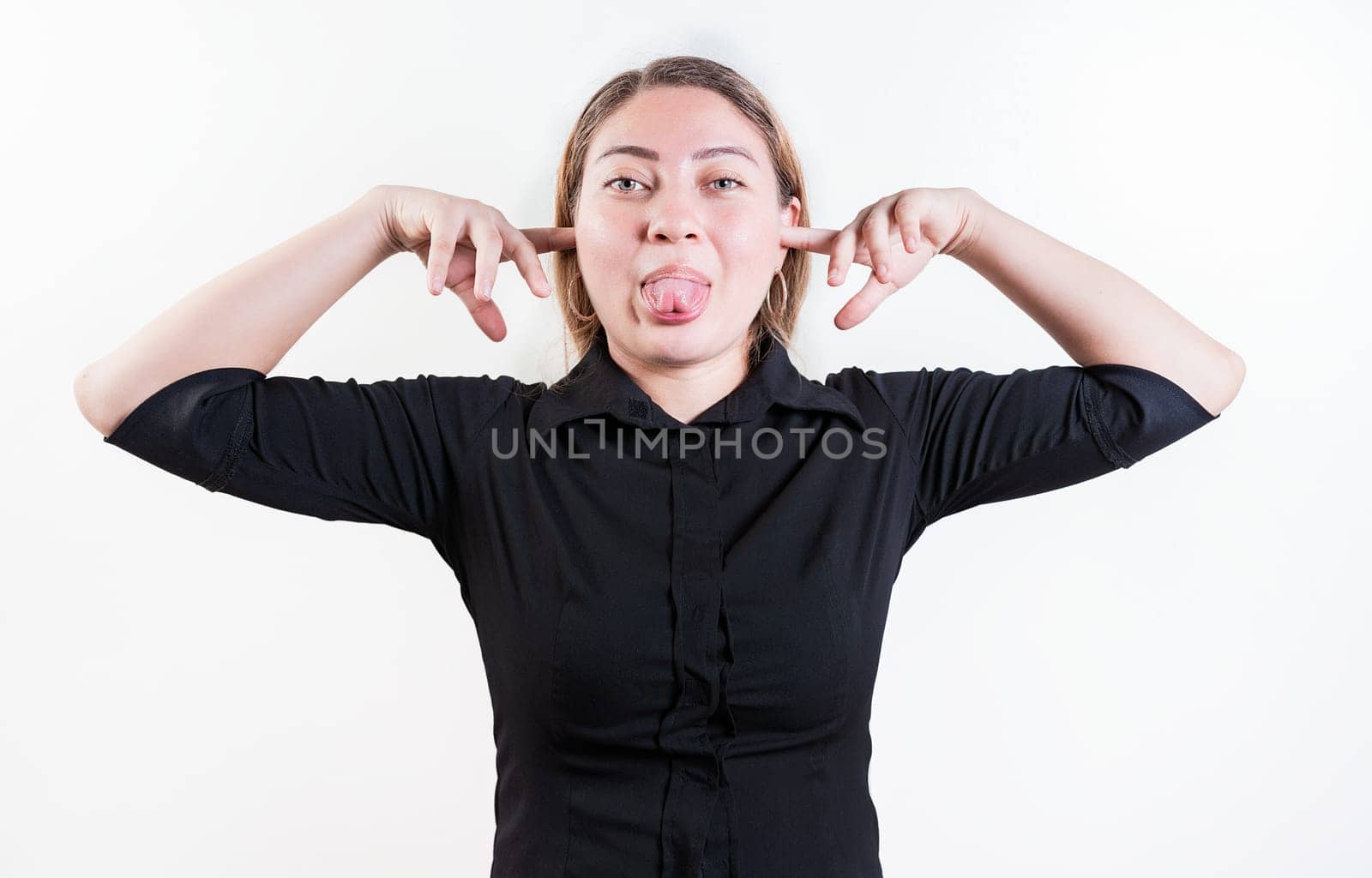 Displeased girl covering ears and sticking out tongue isolated. Young woman covering her ears and making faces isolated