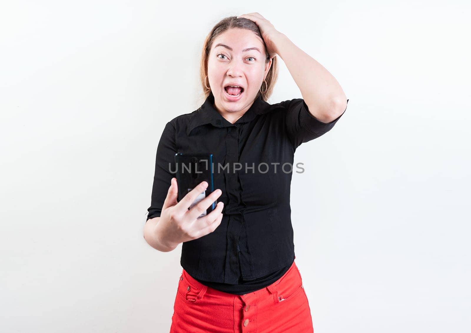 Astonished girl with cell phone holding head isolated. Young woman stunned holding head and cell phone with copy space by isaiphoto