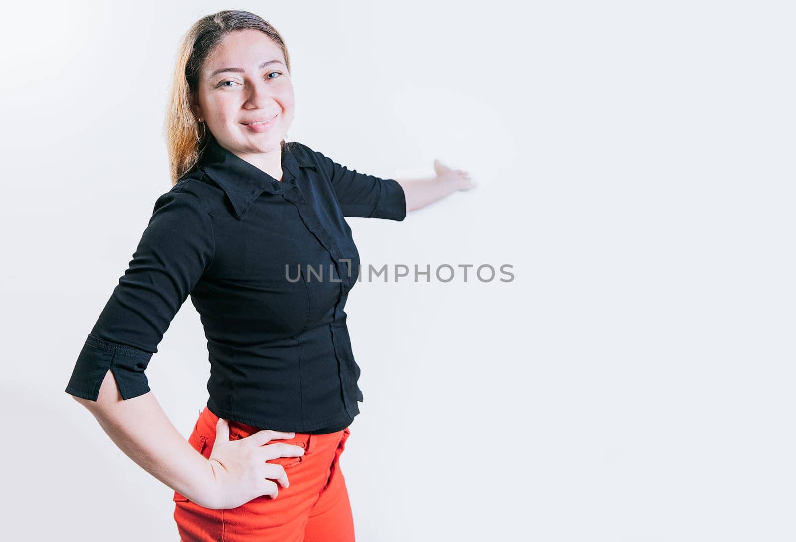 Smiling latin woman welcoming you isolated. Cheerful people pointing a promotion with her palm. Happy young girl pointing back presenting a product by isaiphoto