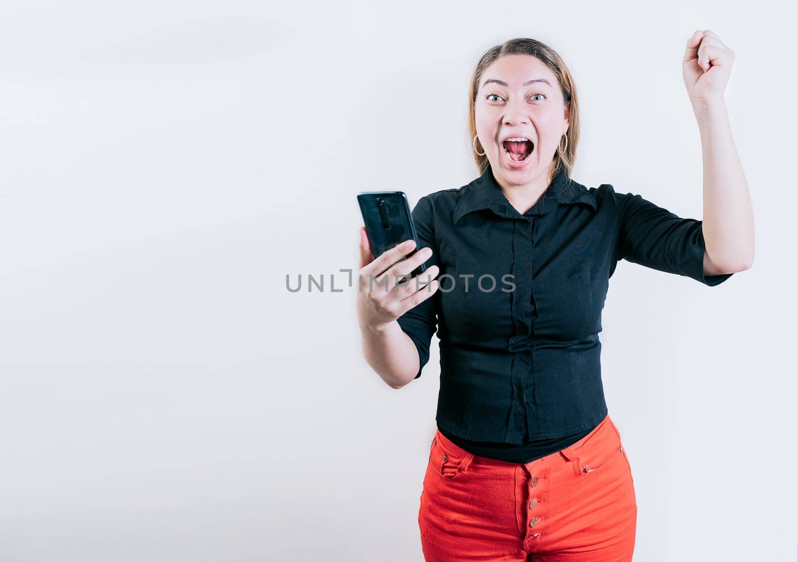 Winner happy young girl holding cell phone. Happy young woman celebrating with phone isolated. Happy people holding smartphone and celebrating by isaiphoto