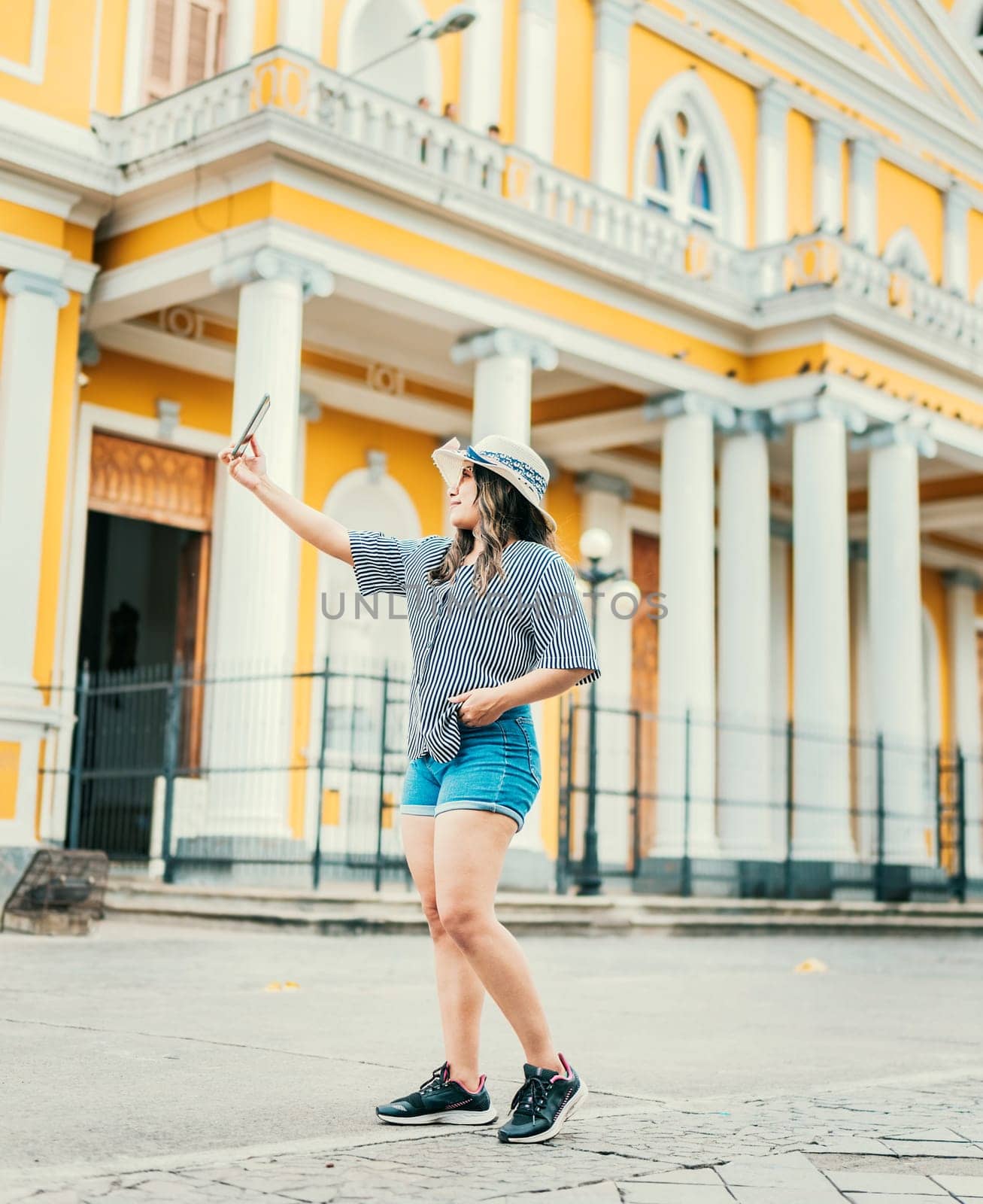 Beautiful tourist in hat taking selfie in the cathedral of Granada. Young travel woman taking a selfie in a public square by isaiphoto