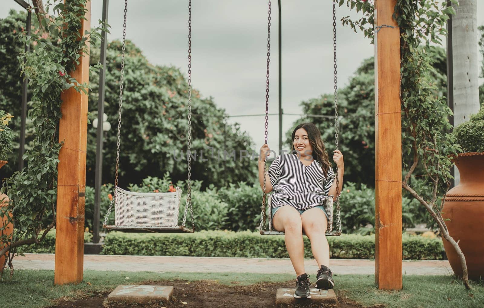 Portrait of smiling girl sitting on a swing in a garden. Happy young woman sitting on a swing in a beautiful garden. by isaiphoto