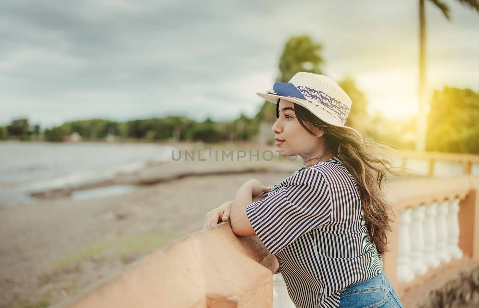 Beautiful tourist girl in hat looking at the beach from a pier. Portrait of female traveler on a pier looking at the horizon by isaiphoto