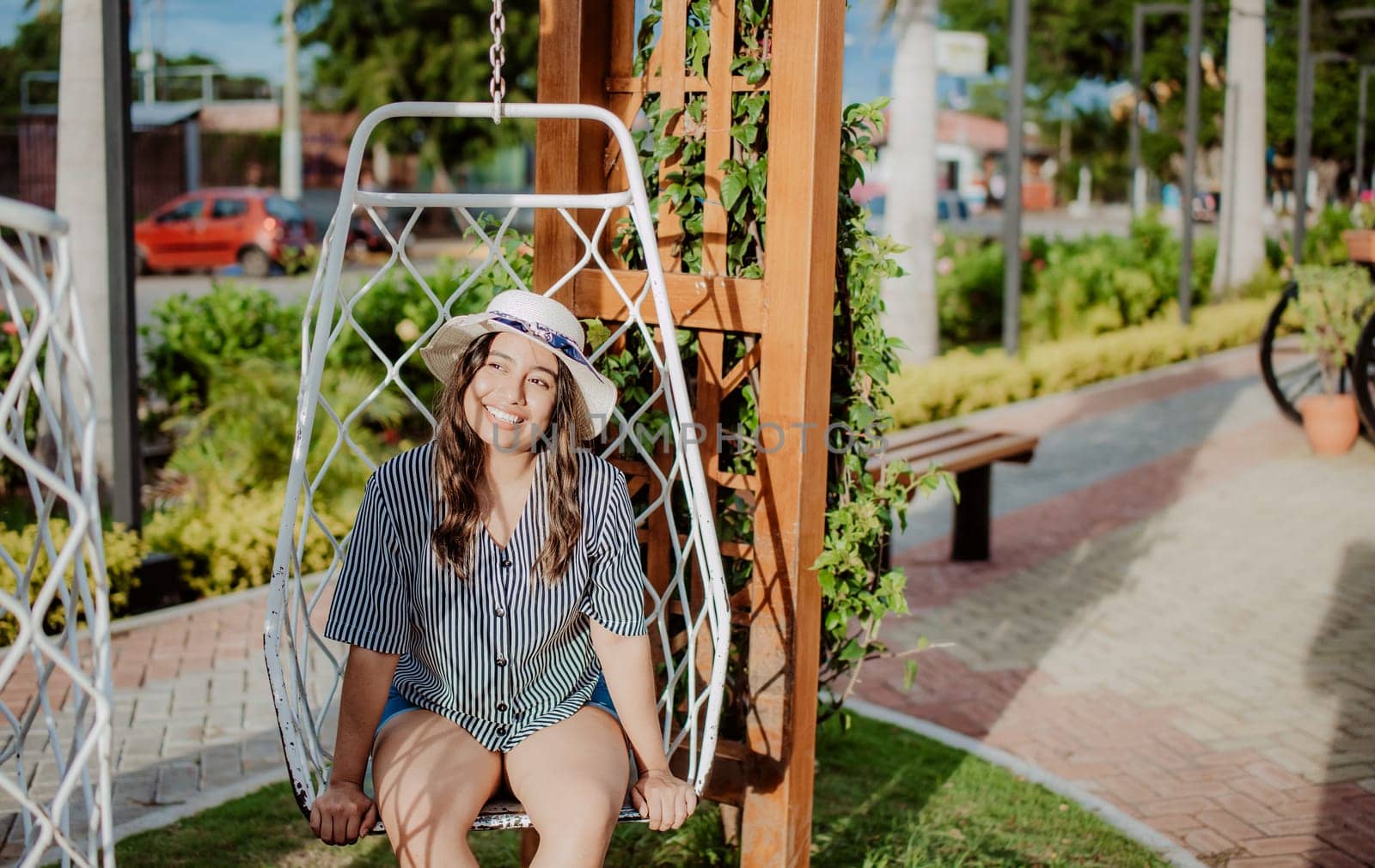 A smiling girl sitting on a swing in La Calzada, Granada, Nicaragua. Relaxed girl in hat sitting on a white swing in a beautiful garden
