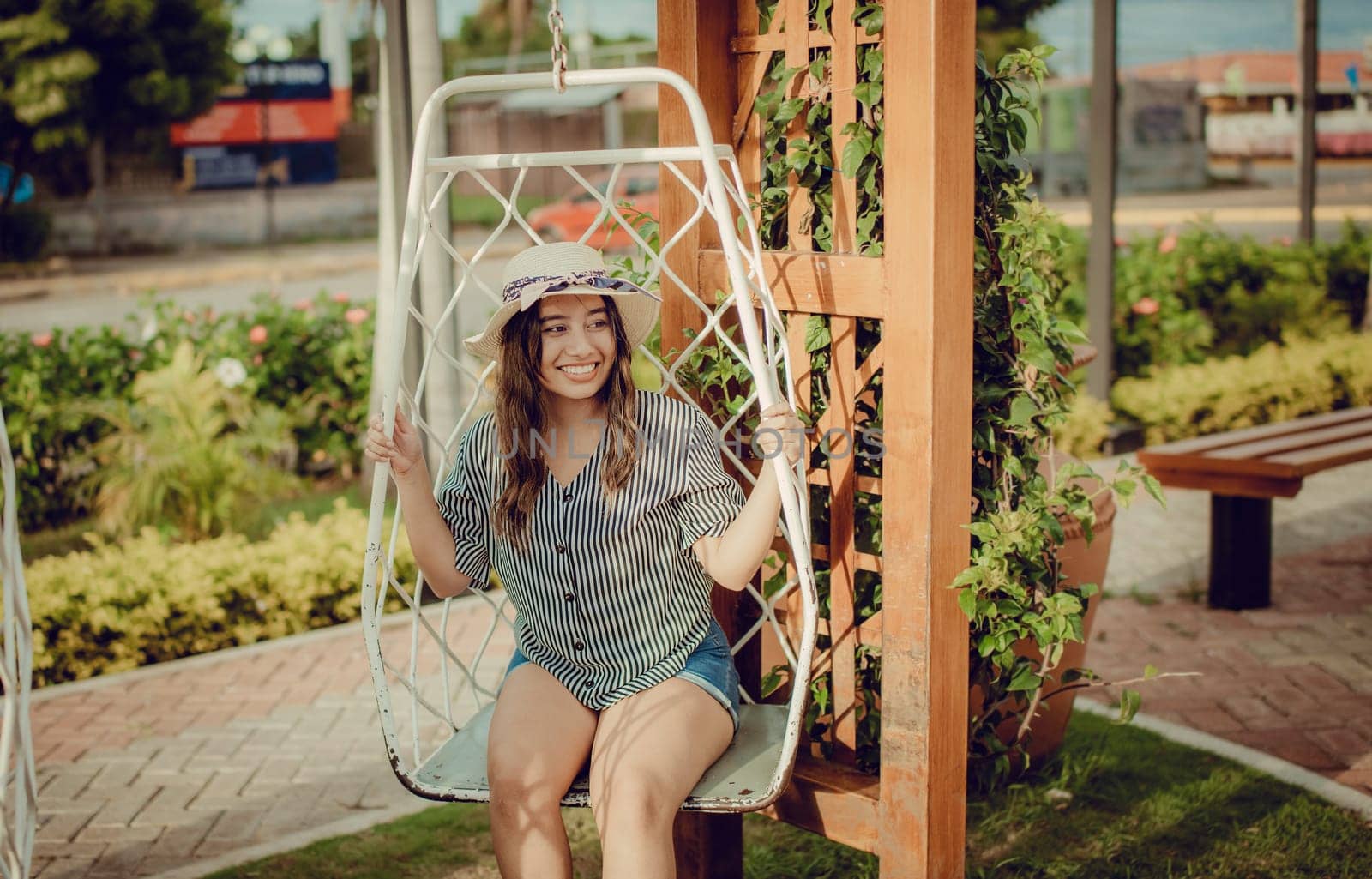 Relaxed girl in hat sitting on a white swing in a beautiful garden. A smiling girl sitting on a swing in La Calzada, Granada, Nicaragua by isaiphoto