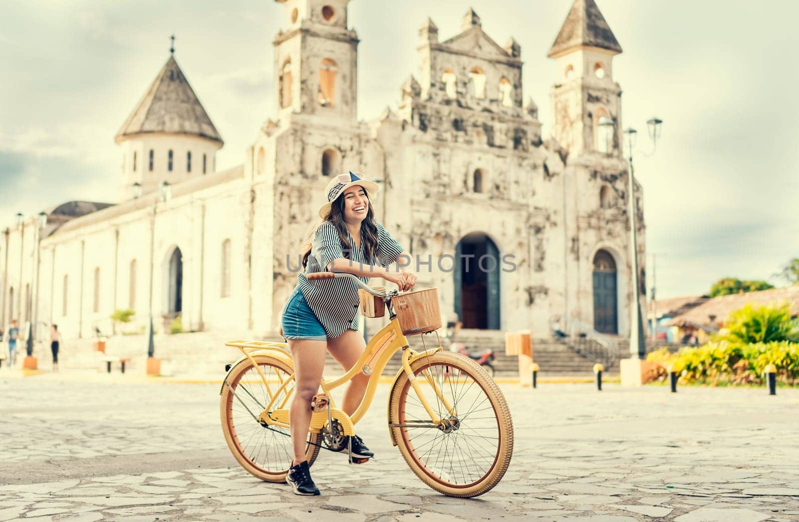 Lifestyle of a happy girl in hat on bicycle on the street. Granada, Nicaragua. Happy girl in hat riding a bicycle at sunset. Tourism and travel concept by isaiphoto