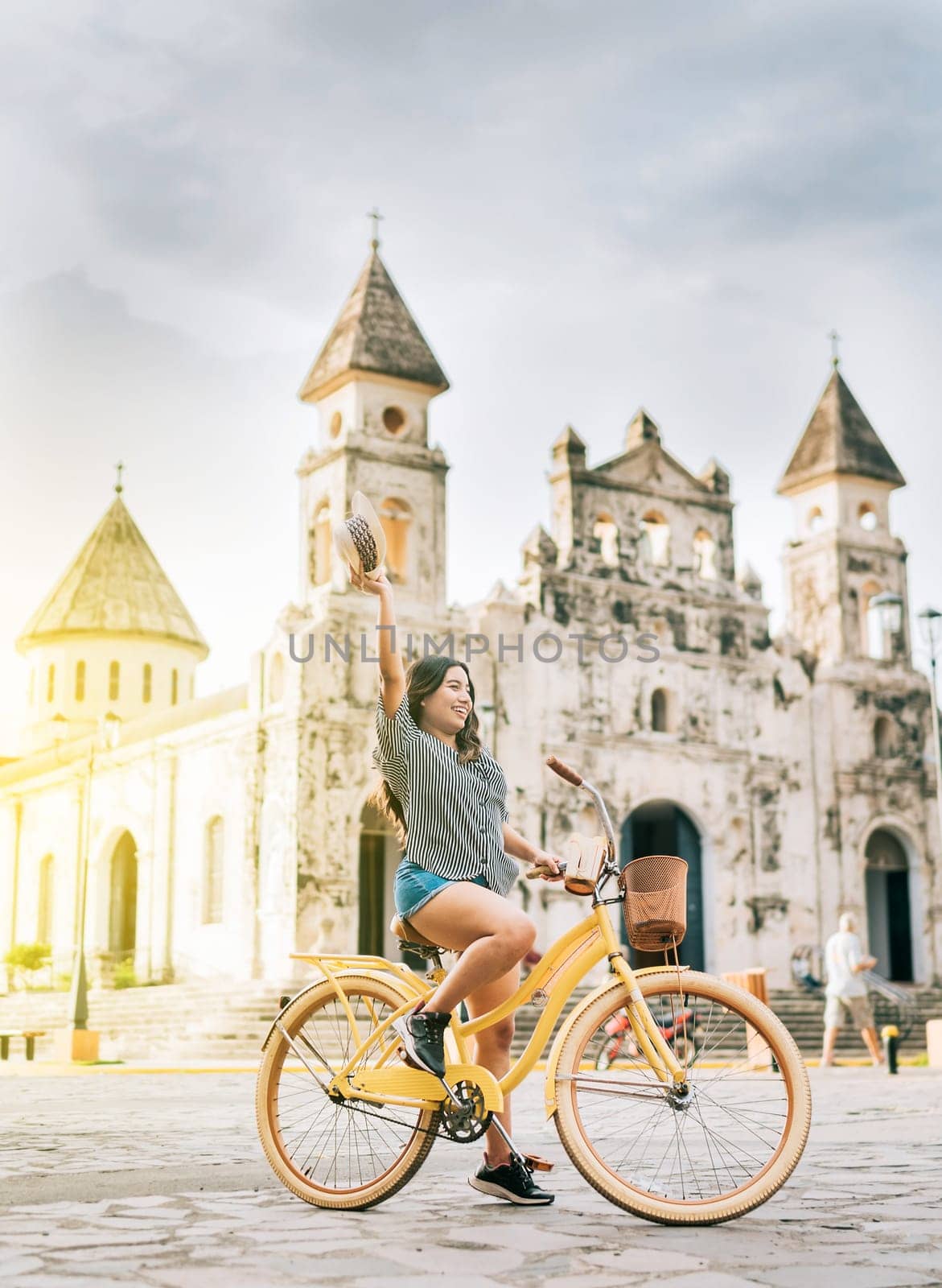 Happy young woman in hat riding a bicycle on the street. Granada, Nicaragua. Lifestyle of a happy girl riding a bicycle holding her hat on the street. Tourism concept