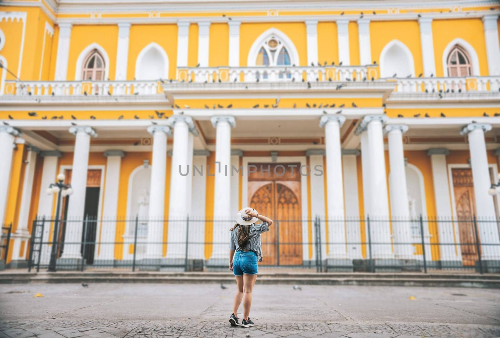 Rear view of tourist girl looking at cathedral. Tourist woman from back looking at a cathedral in a square. Granada, Nicaragua by isaiphoto