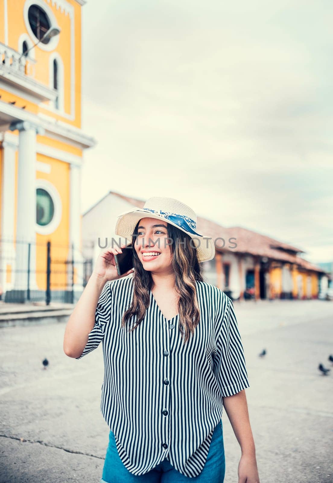 Happy travel woman calling on the phone in a tourist plaza. Beautiful tourist girl talking on cell phone in the square. Granada, Nicaragua by isaiphoto