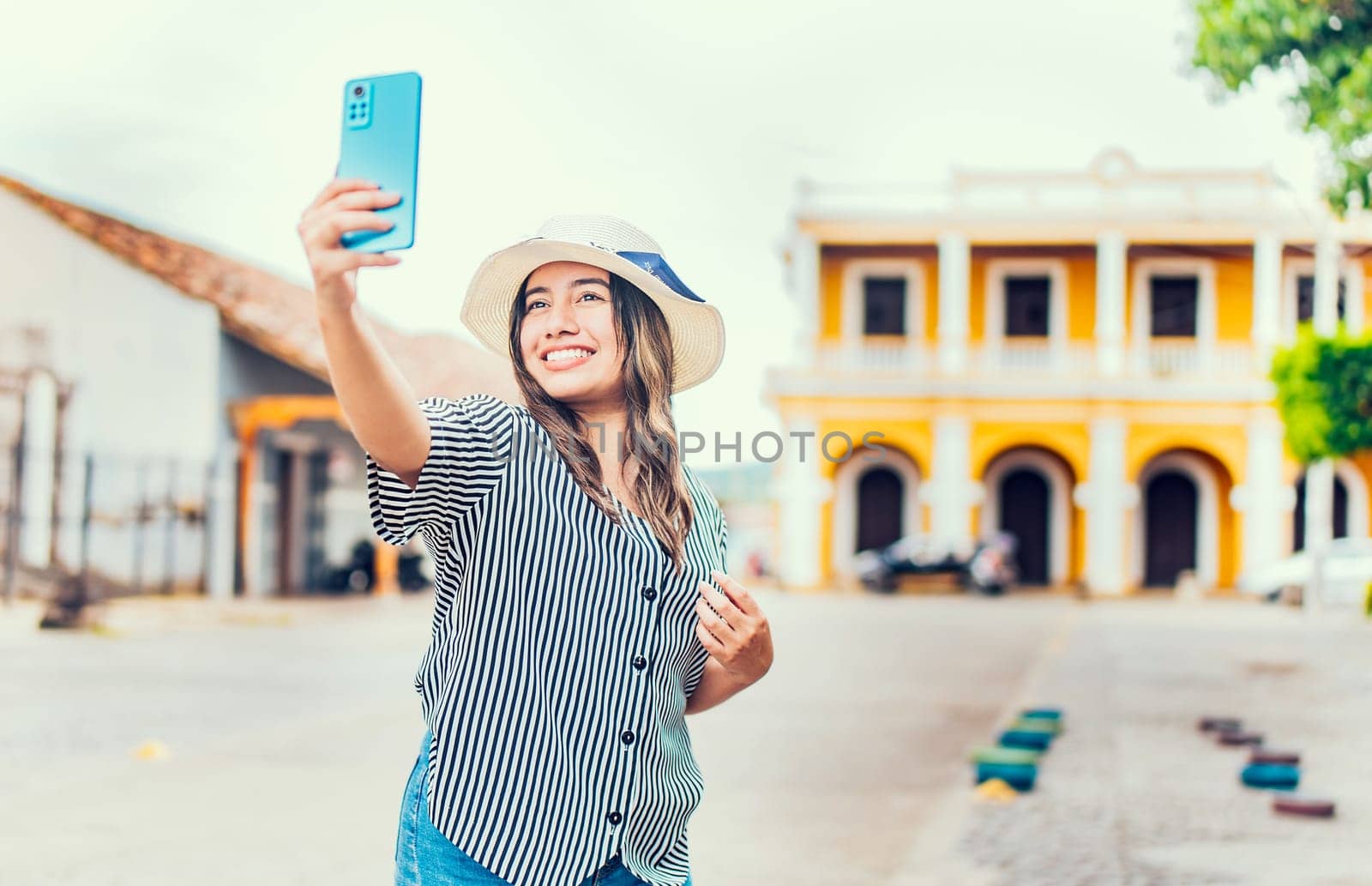 Happy tourist girl taking selfie in the cathedral of Granada. Young travel woman with hat taking a selfie in a square by isaiphoto